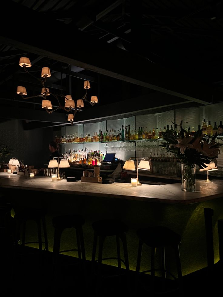 a dimly lit bar with many bottles on the shelves and lamps hanging from the ceiling