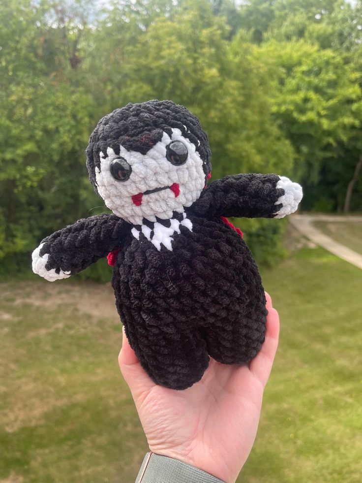 a hand holding a small black and white crocheted stuffed animal in front of some trees