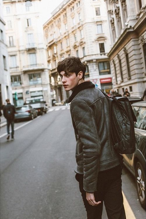 a young man standing on the side of a street next to a car and buildings