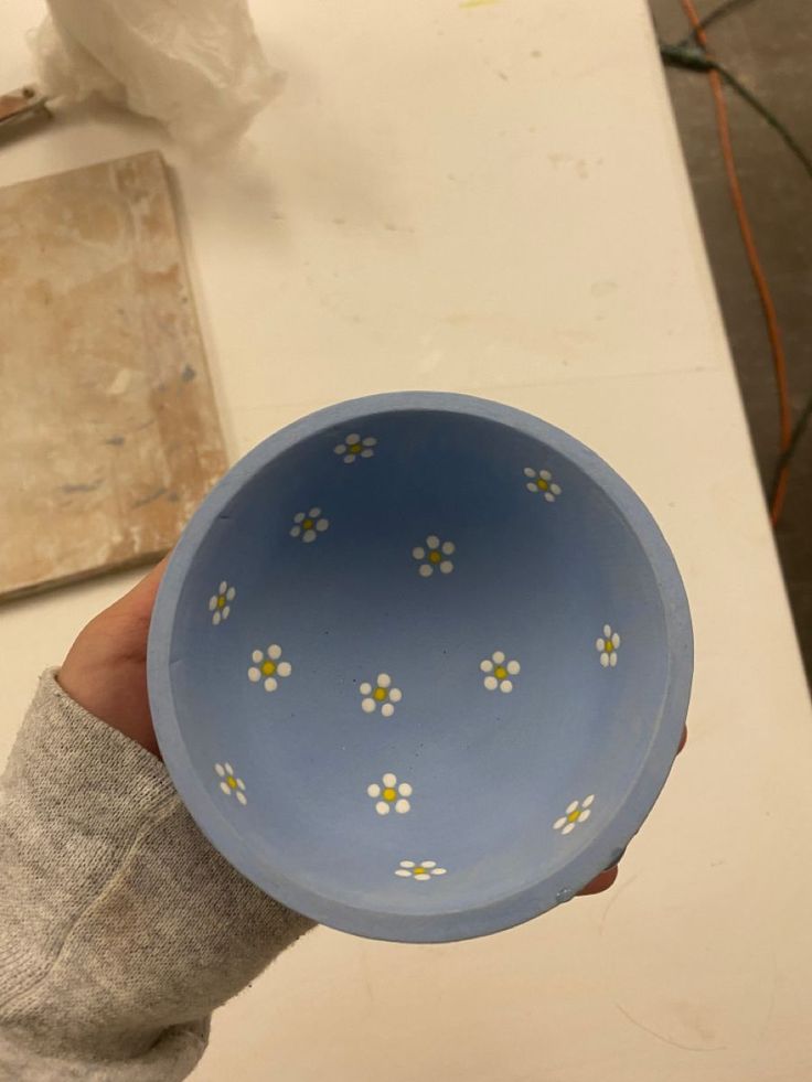 a hand holding a blue bowl with white and yellow flowers painted on the inside of it