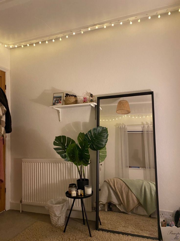 a room with a mirror, plant and lights on the wall next to an ironing board