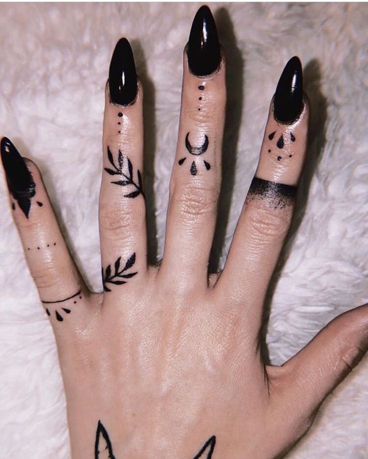 a woman's hand with black nail polish and tattoos on her fingers, which are decorated with leaves