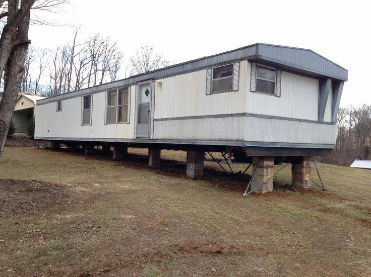 a mobile home sitting on the back of a truck in a grassy field next to trees