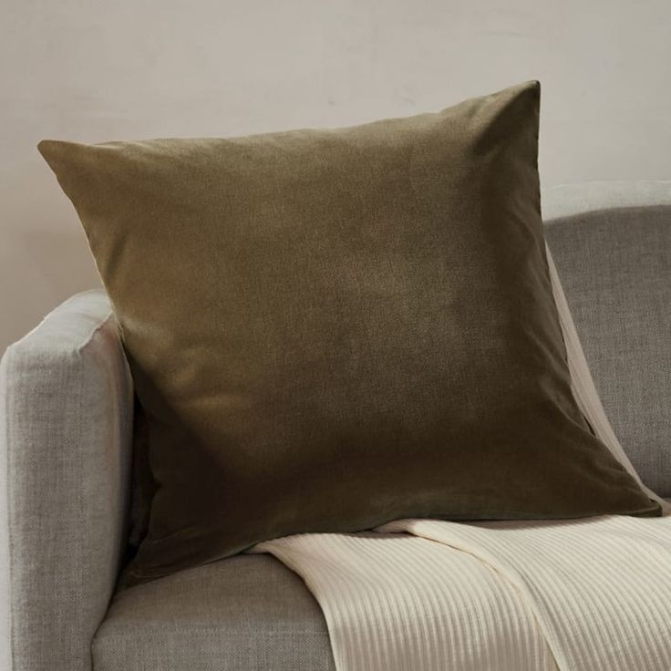 a couch with a pillow on it next to a white wall and a beige chair