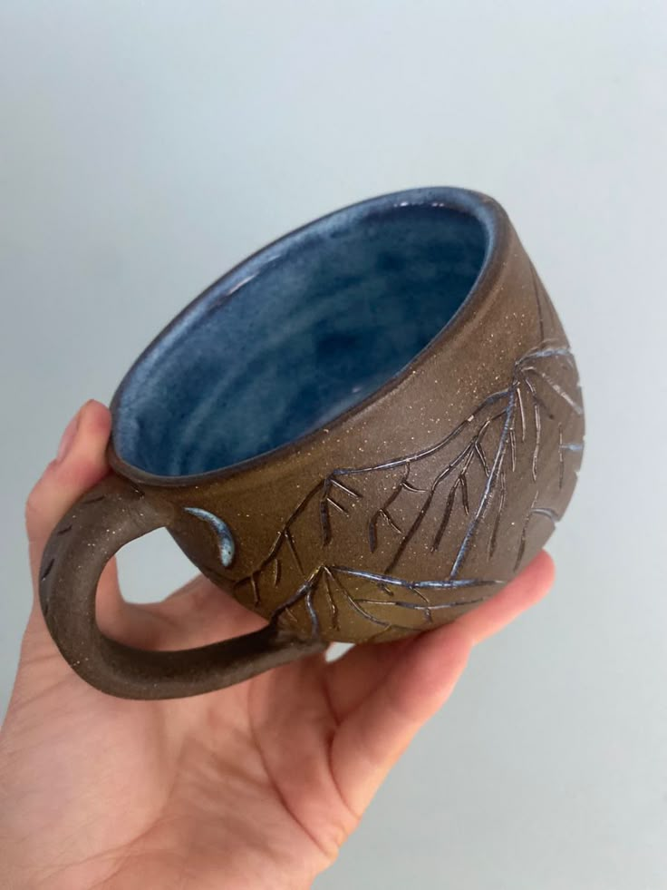 a hand holding a brown and blue cup with designs on it's outside rim