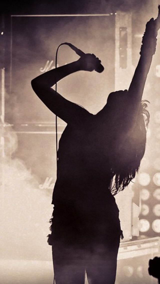 the silhouette of a woman singing on stage with her arms in the air and microphone to her side