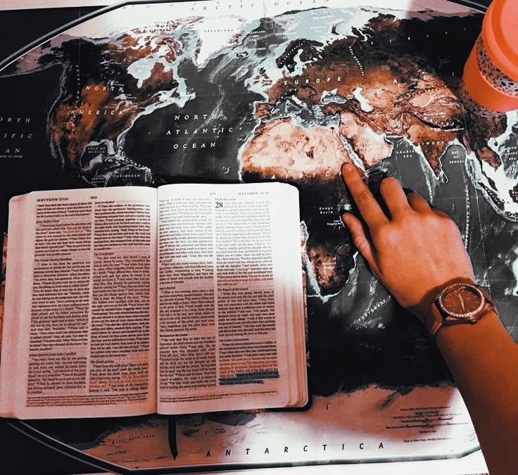 a person reading a book on top of a table with a world map in the background