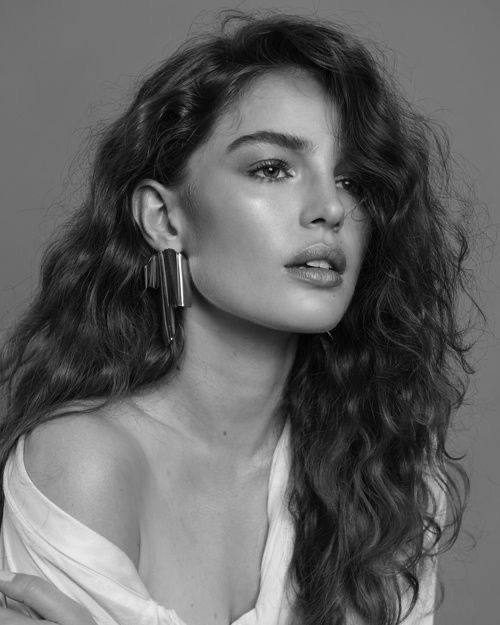 a woman with long curly hair wearing earrings and a white shirt is looking off to the side