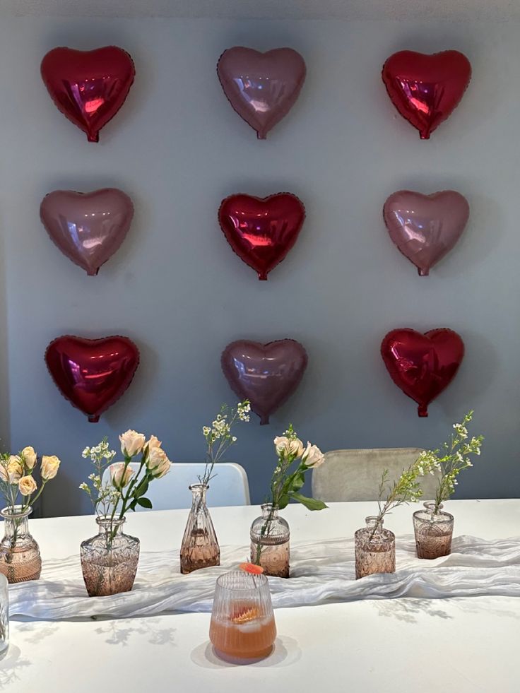 several vases filled with flowers on top of a table next to heart shaped balloons