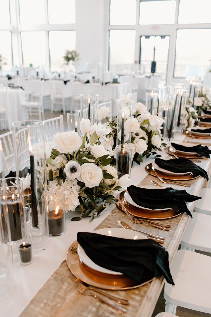 the table is set with black and white plates, napkins, silverware, and flowers