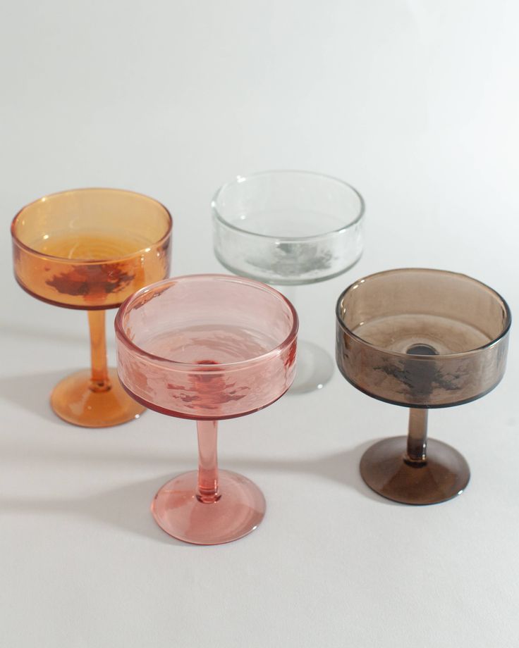 three different colored wine glasses sitting next to each other on top of a white surface