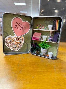 an open tin box with books inside on a wooden table in front of some bookshelves