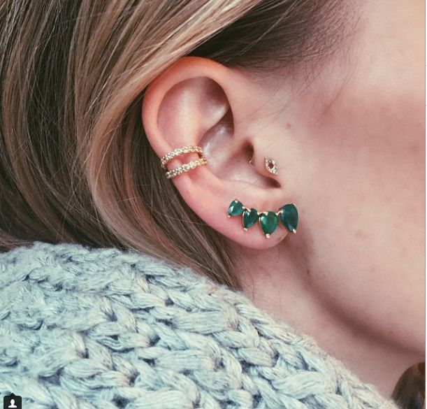 a close up of a person wearing ear piercings with green stones on their ears