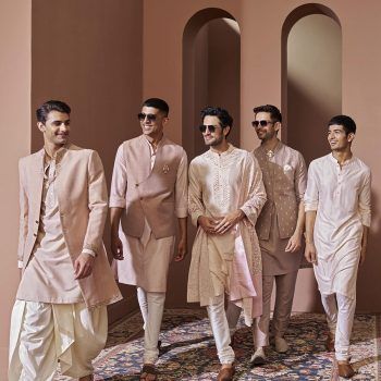 several men in white and beige outfits walking down a carpeted area with pink walls