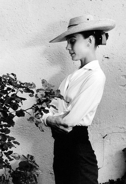 black and white photograph of a woman wearing a hat standing in front of a plant