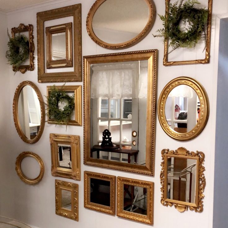 there are many mirrors on the wall with gold frames around them and wreaths hanging above