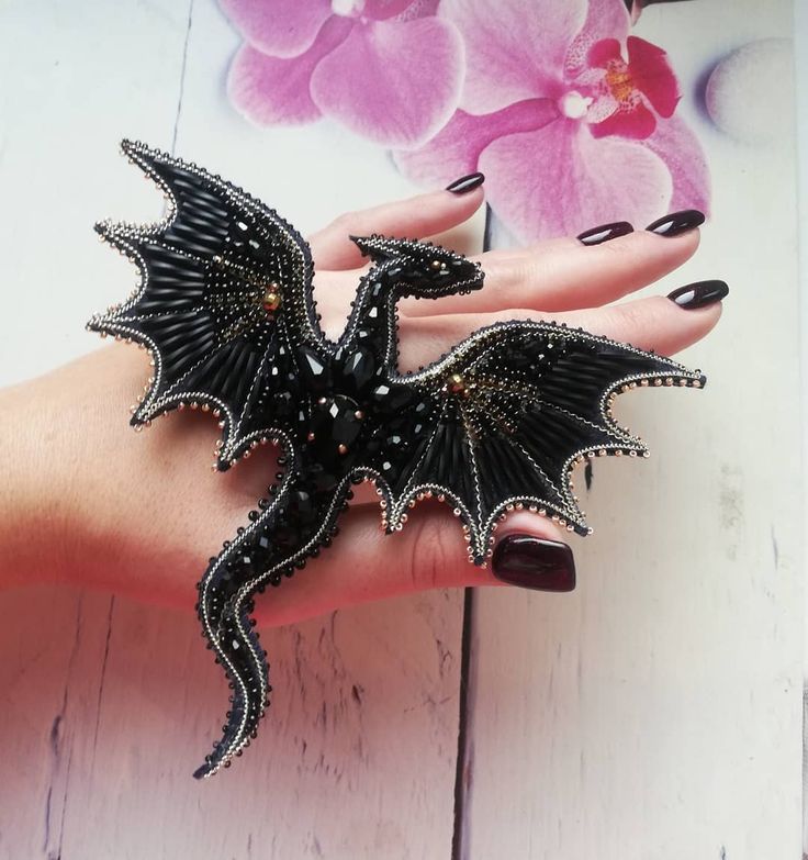 a woman's hand with a black dragon ring on it, and a pink flower in the background