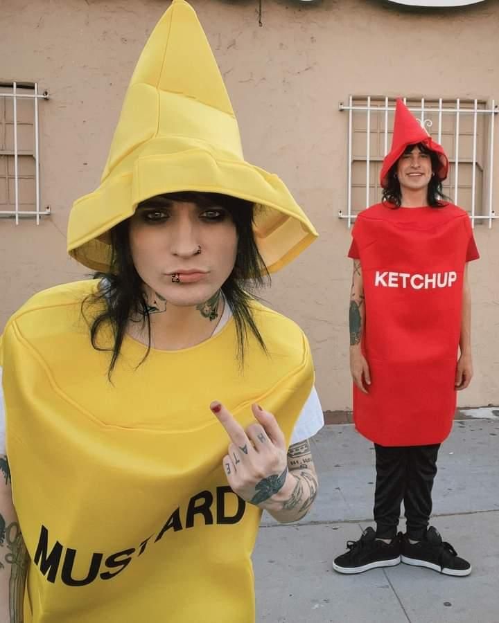 two people dressed in costumes standing on the sidewalk and one is wearing a ketchup shirt