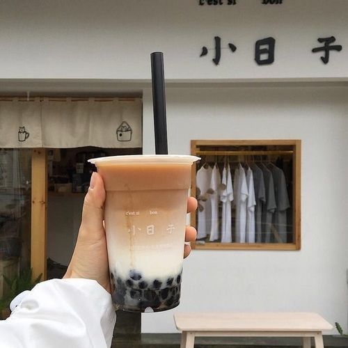 a person holding up a drink in front of a building with chinese writing on it