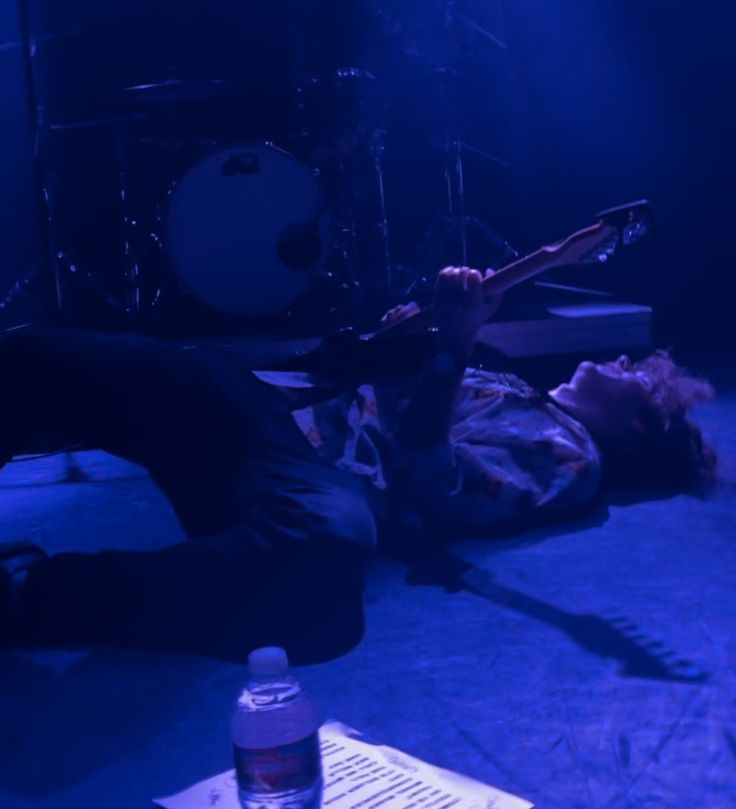 a man laying on the floor with his guitar in front of him and another person lying down next to him