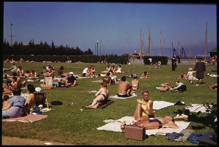 many people are sitting in the grass on towels