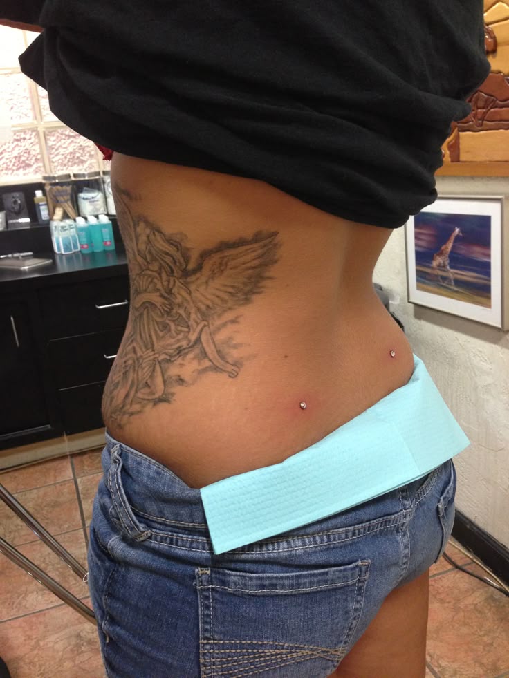 a woman with a bird tattoo on her stomach and lower back, standing in front of a mirror