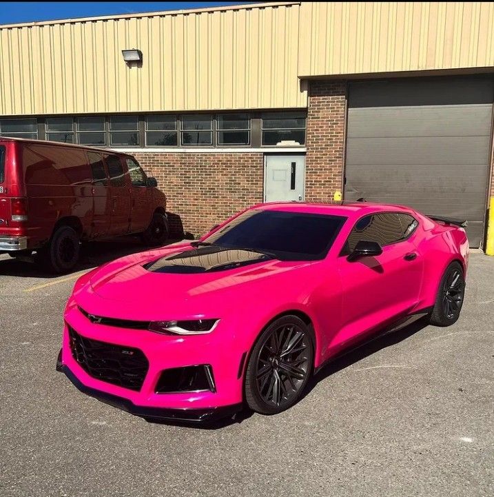 a pink chevrolet camaro parked in front of a building