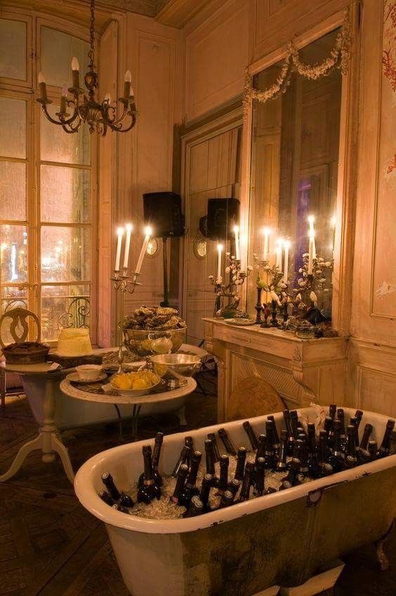 a bath tub filled with lots of bottles next to a table full of food and candles