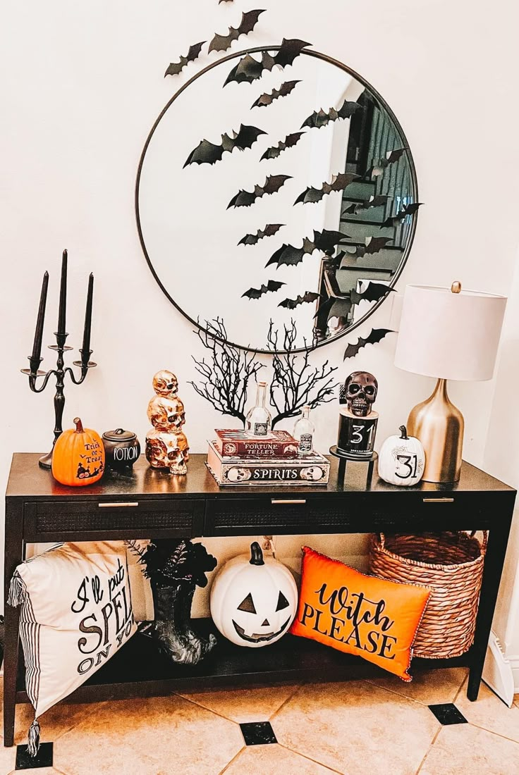 a console table with halloween decorations on it and a round mirror behind it that has bats flying over the top