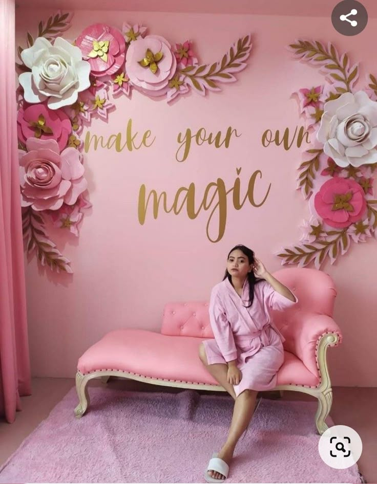 a woman sitting on top of a pink couch in front of a wall with flowers