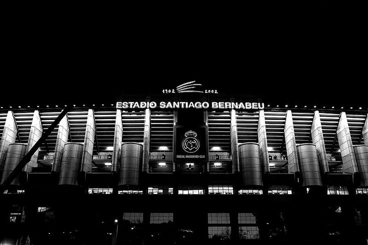 a black and white photo of the outside of a stadium at night with lights on