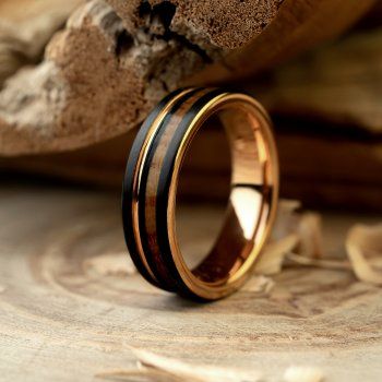 a gold ring with black wood inlays sits on top of a piece of wood