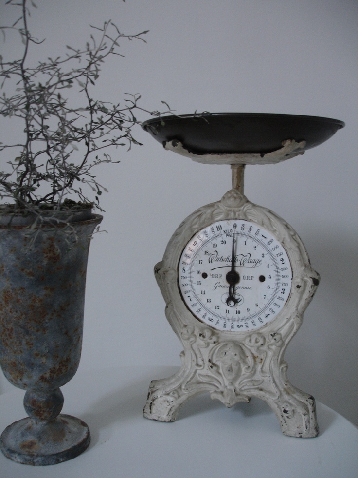 an old white clock sitting next to a vase with a plant in it on a table