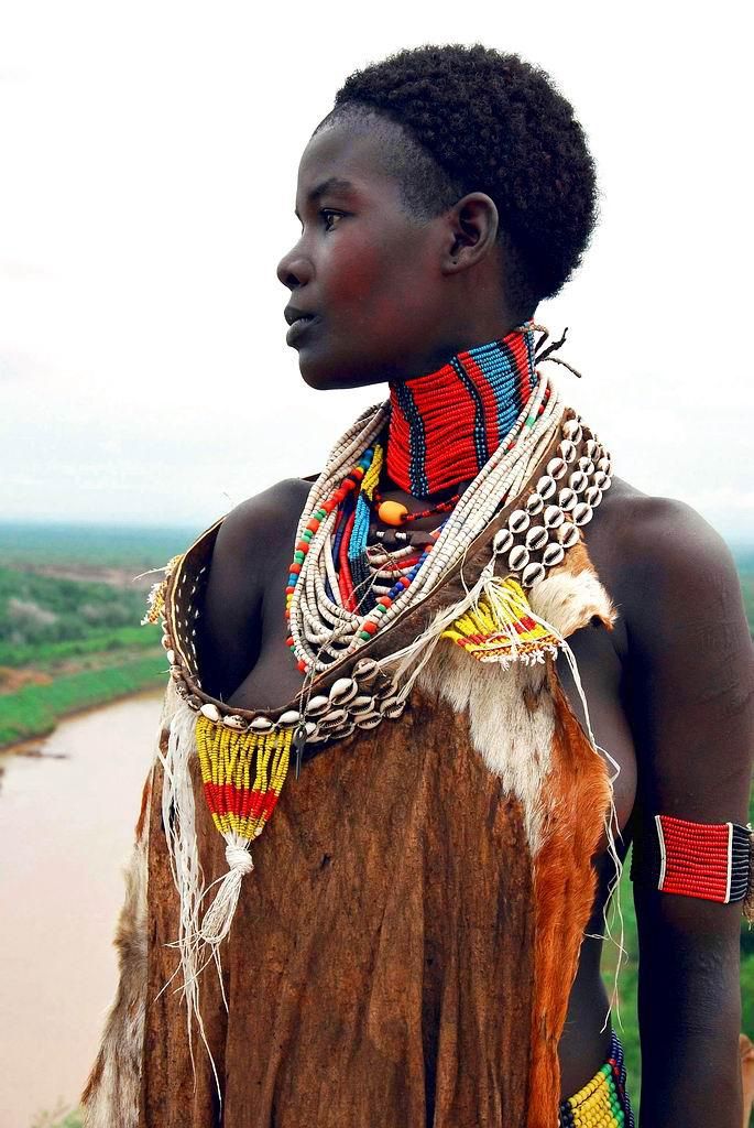 an african woman in traditional clothing and jewelry looks off into the distance with her hand on her hip