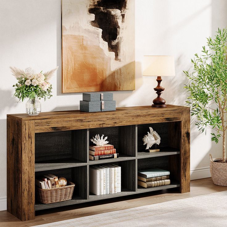 a wooden shelf with books and vases on it in front of a large painting