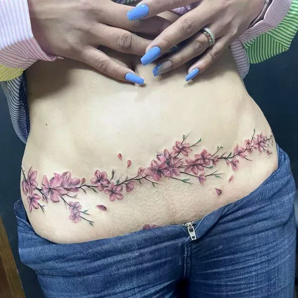 a woman's stomach with pink flowers and leaves on the side, while her hands are