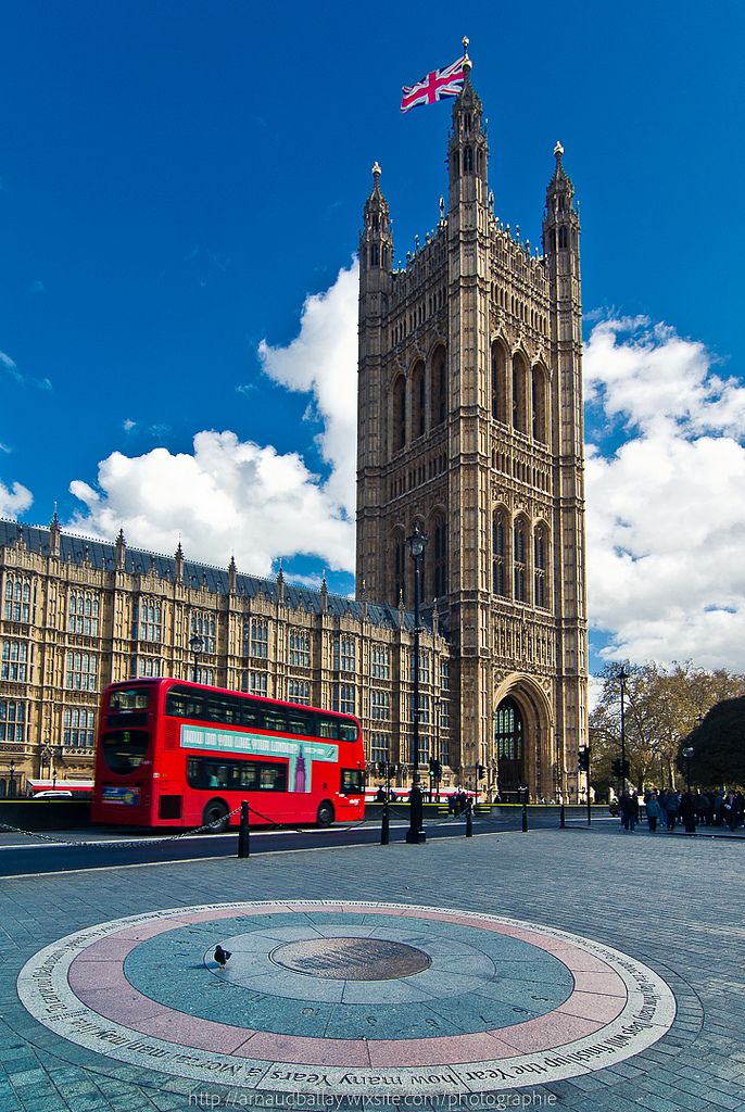 a red double decker bus parked in front of a large building with a clock tower