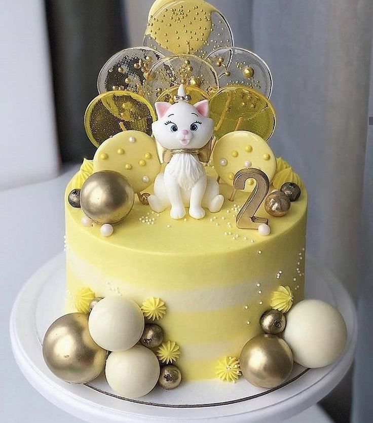 a yellow cake with white frosting and gold decorations on the top is decorated with a cat figurine