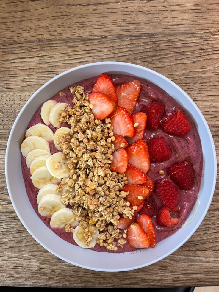 a bowl filled with fruit and granola on top of a wooden table