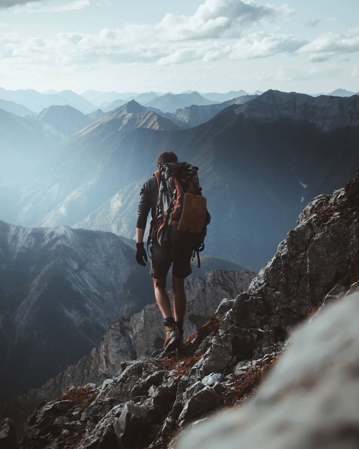 a man hiking up the side of a mountain on top of a rocky hill with mountains in the background