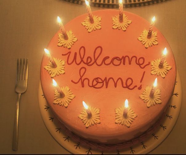 a welcome home cake with lit candles on it