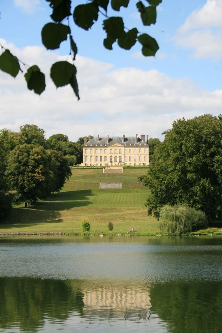 a large house sitting on top of a lush green field next to a lake in front of it