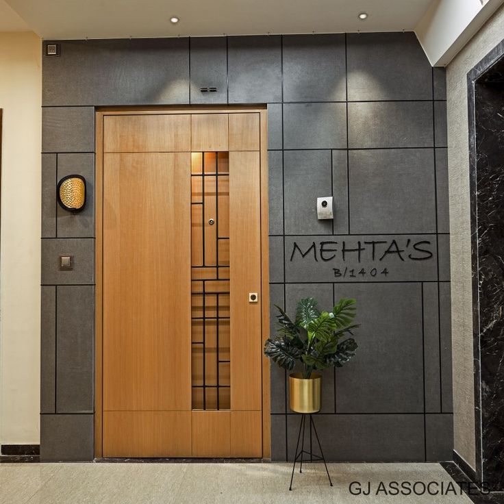 a large wooden door sitting next to a plant in front of a gray and black wall