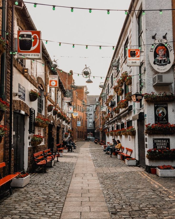 an empty street with benches and lights strung over it's side walk, surrounded by brick buildings