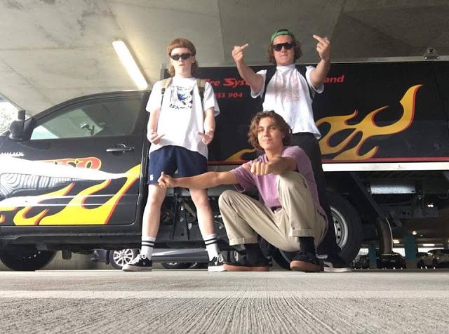 three people standing in front of a van with flames on the side and one person kneeling down