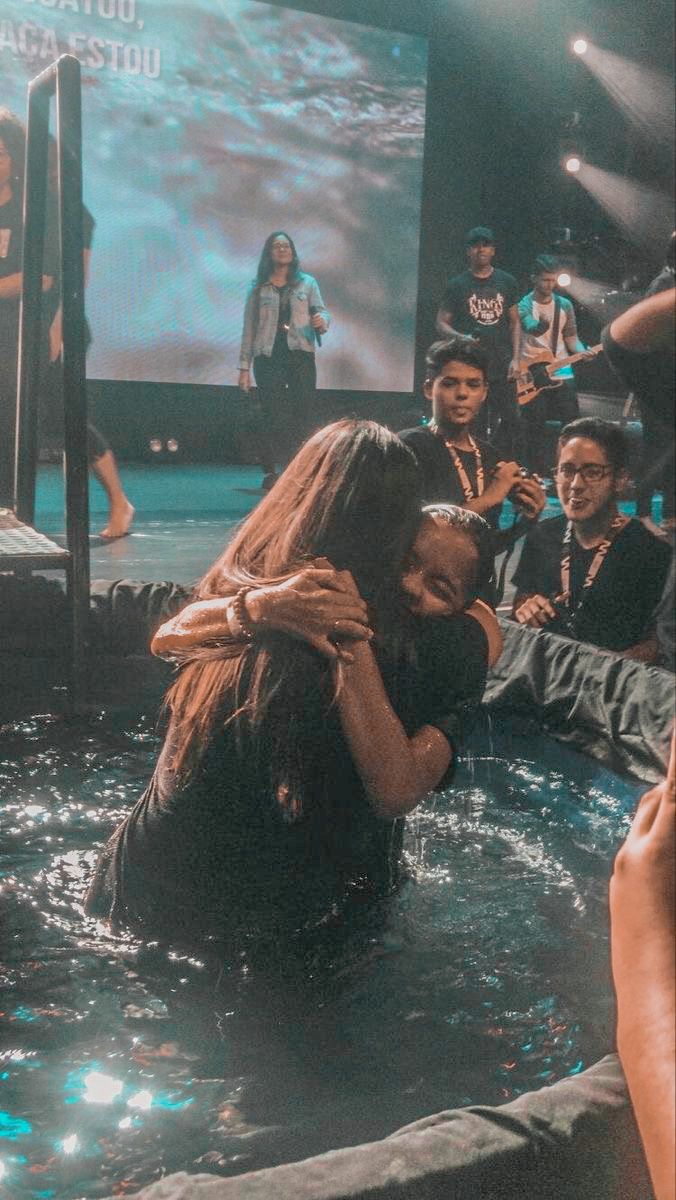 two people are hugging in the water with other people behind them and one person is taking a photo