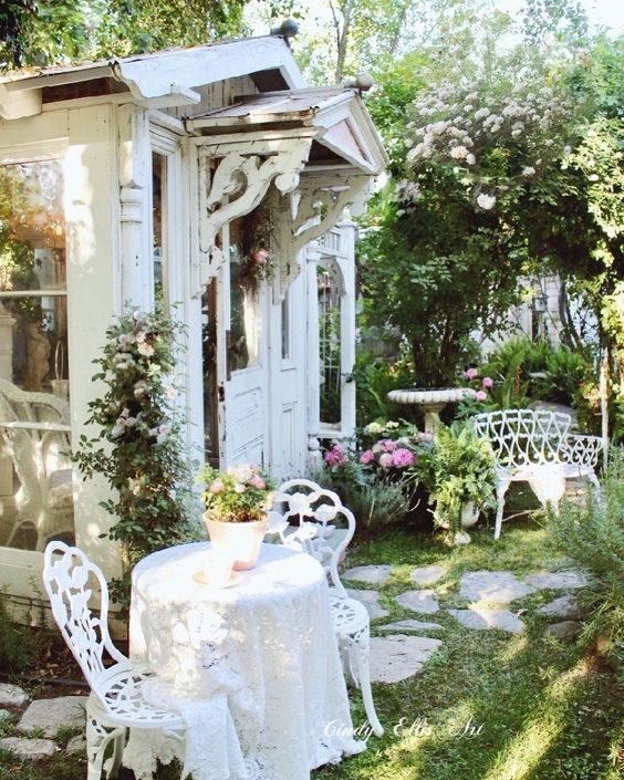 an outdoor dining area with white furniture and potted plants on the table, in front of a shed