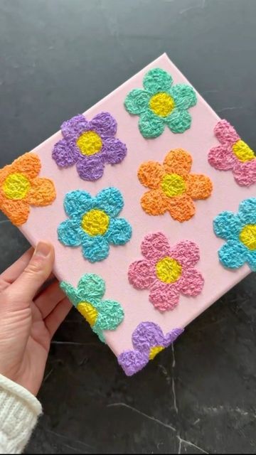 a hand is holding up a small square decorated with flowers