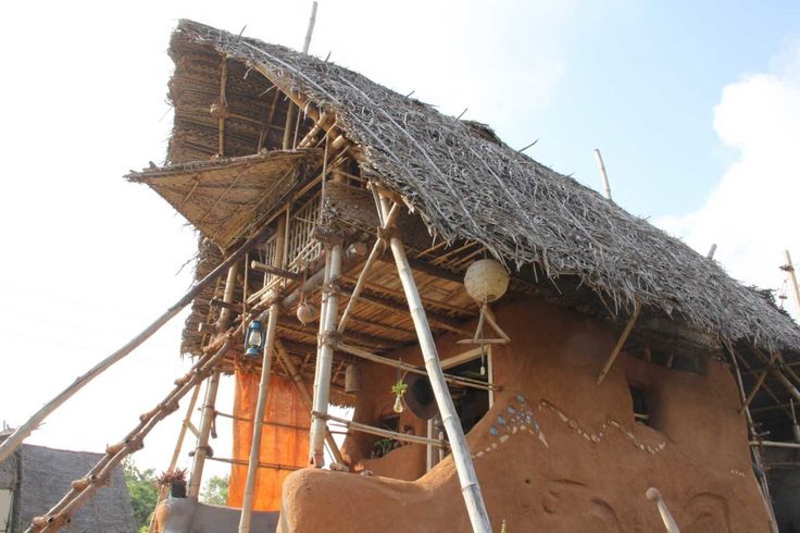 a hut with thatched roof and ladders to the top, in front of a house