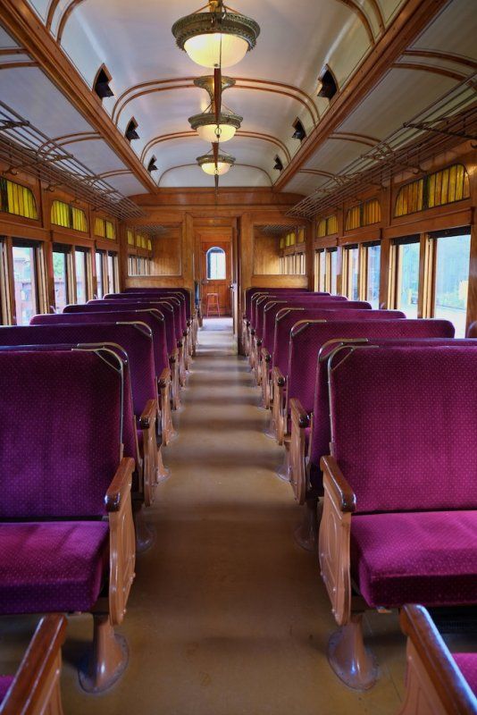 an empty train car with purple seats and wood trimmings on the ceiling is seen in this image